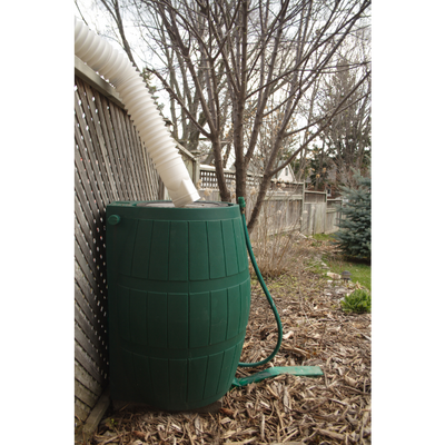 Green rain barrel outside placed along a wooden fence.